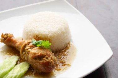 Pişmiş tavuk budu salatalık ve kişniş suyu ile sulu pirinç veya yeşil sebze beyaz tabak ve siyah ahşap masa üzerinde kahvaltı veya öğle ve akşam yemeği için restoranda veya fotokopi salonu olan yemek salonunda