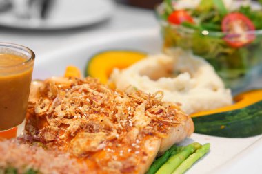 Kızarmış soğanlı somon balığı bifteği ızgara ve beyaz susamlı patates püresi ve balkabağı soslu ve domates sebzeli salatayla diyet deniz ürünleri ve Japon restoranında omega 3 diyet deniz ürünleri.