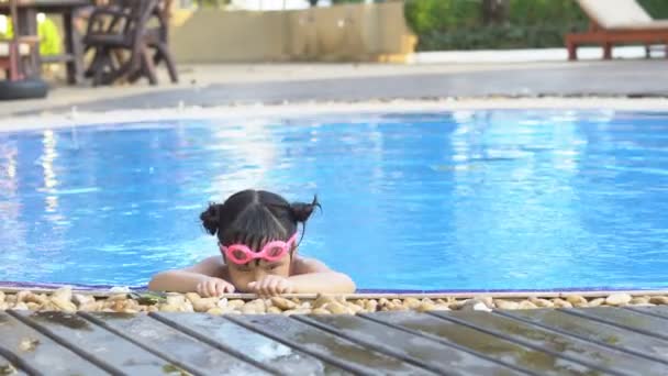 アジアの子供たちかわいいまたは子供の女の子は 夏休みの運動でリフレッシュし リラックスするためのプールやウォーターパークで楽しい水泳や笑顔のためのピンクのビキニとゴーグルを身に着けています4K — ストック動画