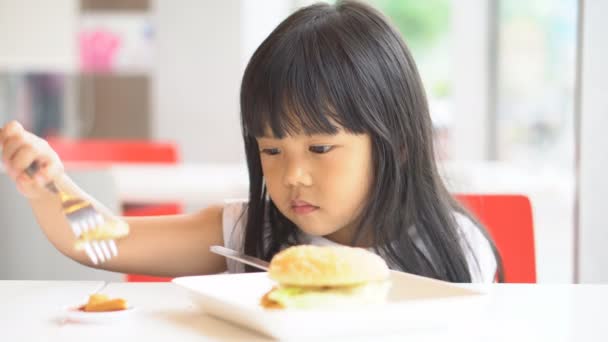 アジアの子供たちかわいいまたは子供の女の子おいしいトマトソースやケチャップとハムバーガーを食べる白い皿やテーブルの上に朝食やランチにナイフを持って楽しいと幸せな笑顔のためのレストランで4K — ストック動画