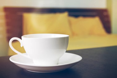 Sıcak kahve ya da çay, beyaz bardakta, sabah yatak odasındaki ahşap masada. Tazelik için.