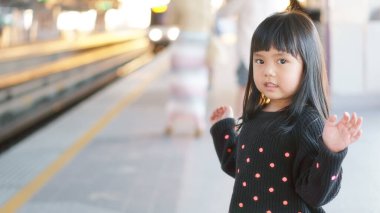 Asian children cute or kid girl waiting sky train on railway station and nature sunlight in the city for travel with space clipart