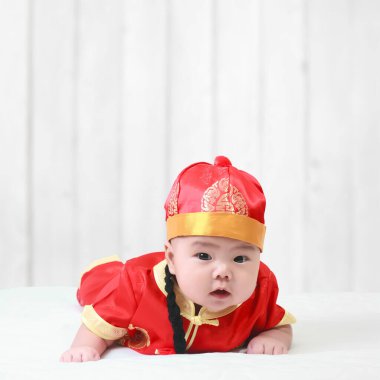 Asyalı neşeli bebek ya da çocuk Çin Yeni Yıl elbisesi giyip mutlu yıllar festivali ve uzay partileri için stüdyoda beyaz ahşap arka planda gülümseyerek eğleniyor.