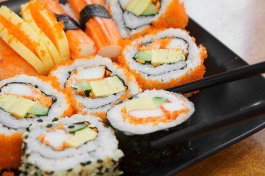 Somon çiğ karides yumurtalı suşi rulosu ve siyah tabakta susam ve öğle yemeğinde çubukla ahşap masa ya da uzay boşluğu olan Japon restoranında akşam yemeği.