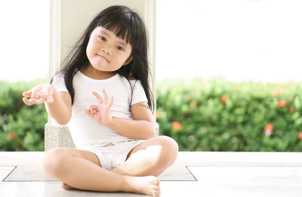 Asian children cute or kid girl sit for meditation or yoga for peace and relax or recreation with cheeky fun in garden pavilion at temple or church and wearing white dress with nature sunlight
