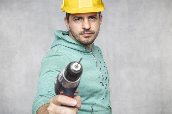 the construction worker holds an electric screwdriver in his han