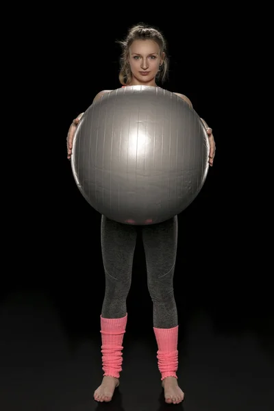 Молодая атлетичная девушка упражняется с большим резиновым мячом — стоковое фото