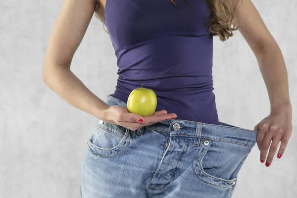 Young athletic female silhouette, apple and old big pants — Stock Photo, Image