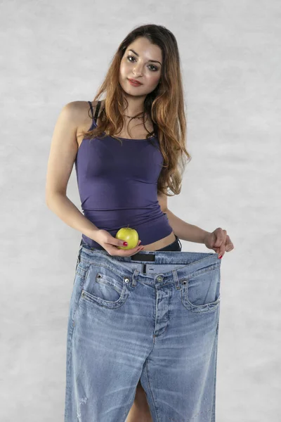 Giovane silhouette femminile atletica, mela e vecchi pantaloni grandi — Foto Stock