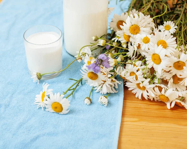 Simply stylish wooden kitchen with bottle of milk and glass on table, summer flowers camomile, healthy foog moring concept