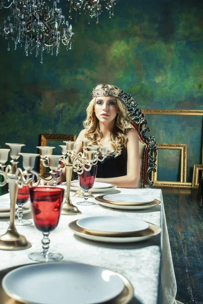young blond woman wearing crown in fairy luxury interior with empty antique frames total wealth, rich lifestyle concept close up