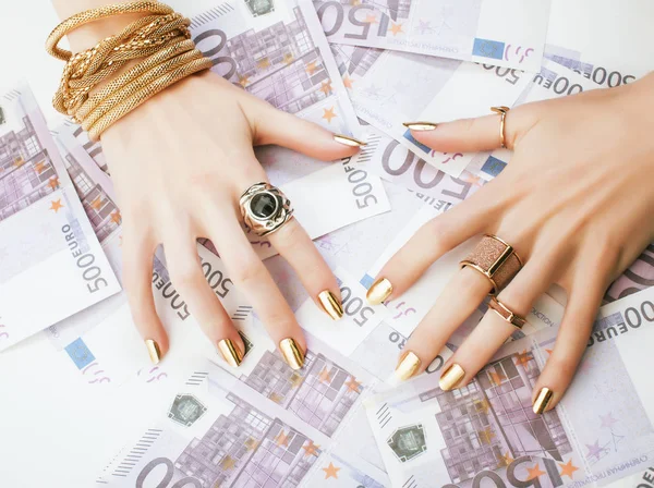 hands of rich woman with golden manicure and many jewelry rings on cash euros close up