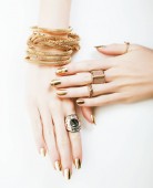 žena ruce se zlatou manikúrou hodně šperků na bílém pozadí zblízka krása koncept