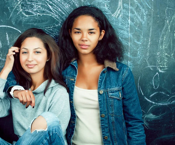 back to school after summer vacations, two teen real girls in classroom with blackboard painted together, lifestyle mixed races people concept