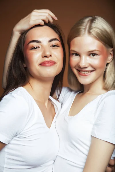 two pretty diverse girls happy posing together: blond and brunette on brown background, lifestyle people concept