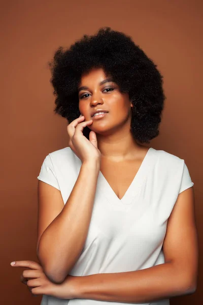 pretty young african american woman with curly hair posing cheerful gesturing on brown background, lifestyle people concept