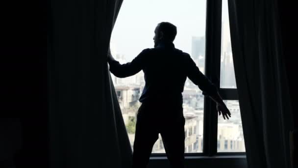 男人揭开窗帘的剪影 从家里的窗户欣赏风景 — 图库视频影像