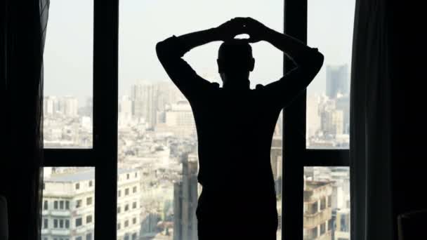 ストレッチ男性のシルエットの腕 首と窓から景色を眺める — ストック動画