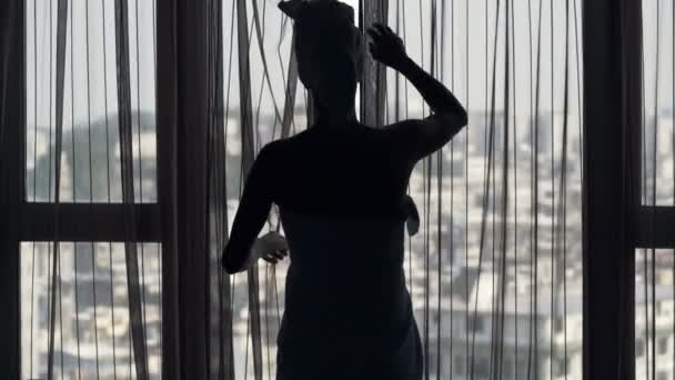 妇女在毛巾揭幕窗帘和欣赏从窗口的看法在家里 — 图库视频影像