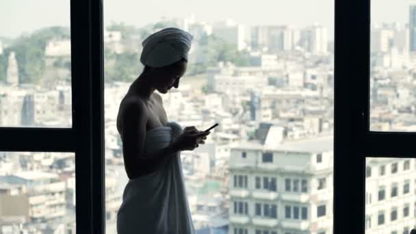 Mujer Joven Mensajes Texto Toalla Teléfono Inteligente Por Ventana Casa — Vídeos de Stock