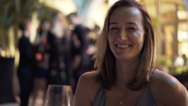 夜カフェに座ってカメラにワインで乾杯を育てる幸せな女性 — ストック動画