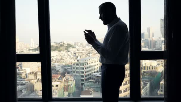成功的商人与智能手机站在一个窗口在办公室 — 图库视频影像