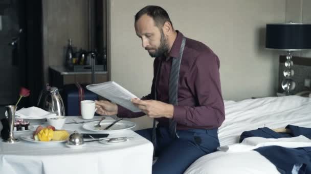 ホテルでの朝食時に雑誌と飲むお茶を読む青年実業家 — ストック動画