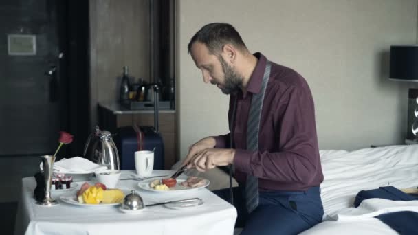 ホテルでベッドの上に座り 朝食を食べる青年実業家 — ストック動画