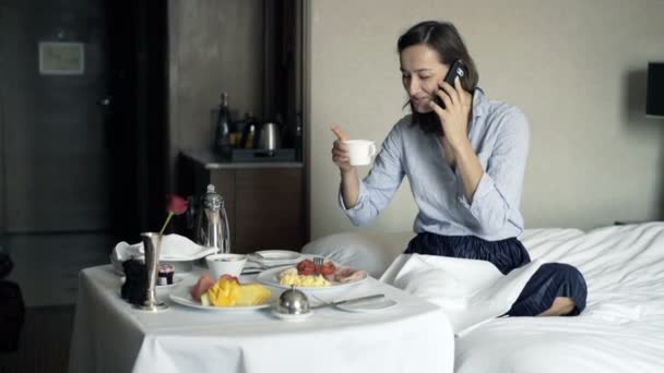 Νεαρός Επιχειρηματίας Μιλάει Στο Κινητό Και Τρώει Πρωινό Στο Ξενοδοχείο — Αρχείο Βίντεο