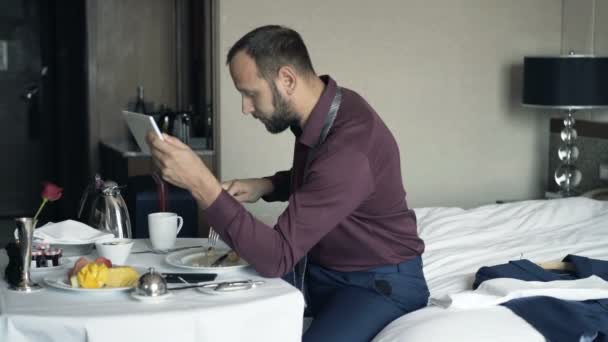 実業家タブレットに映画を見ていると ホテルの部屋で朝食を食べる — ストック動画