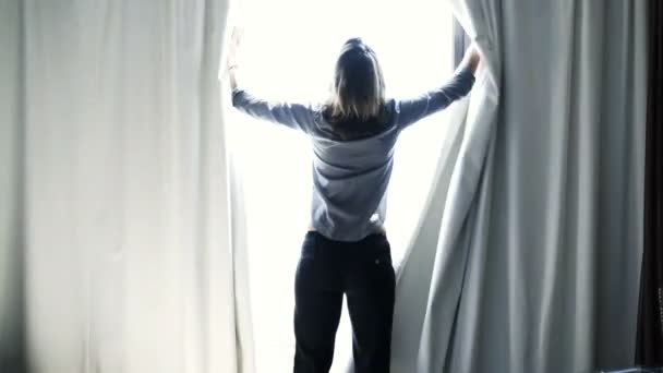 女性はカーテンを発表して自宅の窓から景色を眺める — ストック動画