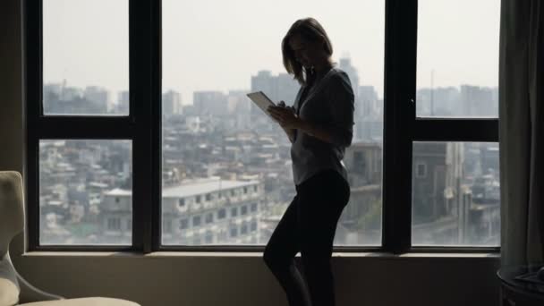 妇女使用平板电脑的剪影在窗口站立在家 — 图库视频影像