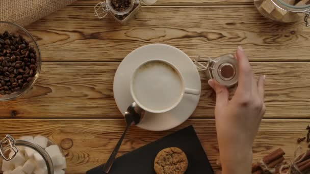 Barista hand, kaffekopp. Kanel, cassia eller muskot pulver läggs till cappuccino. Träskrivbord ovanifrån — Stockvideo