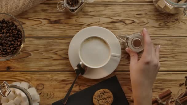 Barista hand, coffee cup. Cinnamon,cassia or nutmeg powder added to cappuccino. Wood desk top view — Stock Video