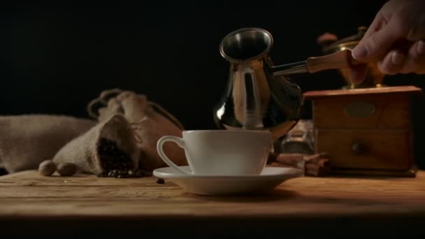 Strong black coffee is poured from cezve into porcelain cup by baristas hand — Stock Video