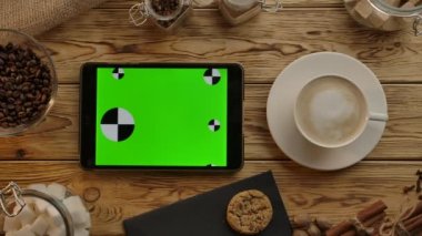 Ahşap masada yatay duran yeşil ekranlı dijital tablet. Ye, iç, çalış.