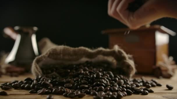 Human hand scattering roasted coffee beans from fistful over burlap sack — Stock Video