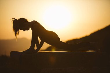 Genç kadın batımında yoga dağda pratiği yapıyor. Pratik yoga açık genç kadın silüeti.
