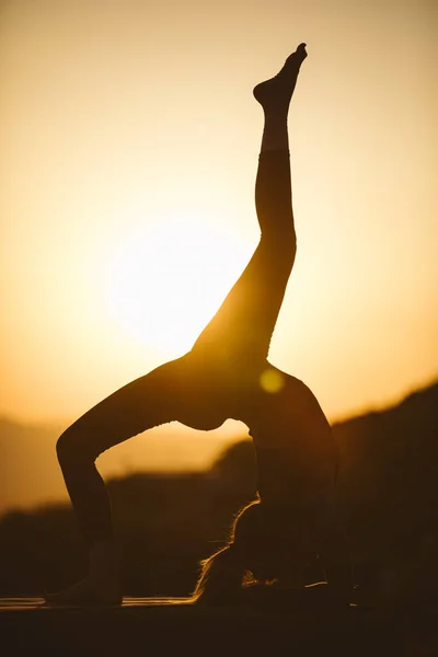 Young woman is practicing yoga on the mountain at sunset. Silhouette of young woman practicing yoga outdoor.