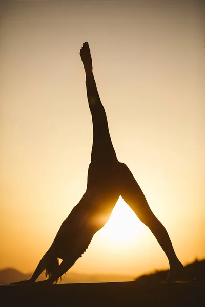 Young woman is practicing yoga on the mountain at sunset. Silhouette of young woman practicing yoga outdoor.