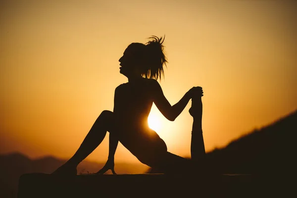 Young woman is practicing yoga on the mountain at sunset. Silhouette of young woman practicing yoga outdoor.