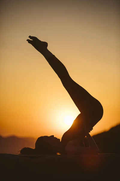 Young woman is practicing yoga on the mountain at sunset. Silhouette of young woman practicing yoga outdoor.