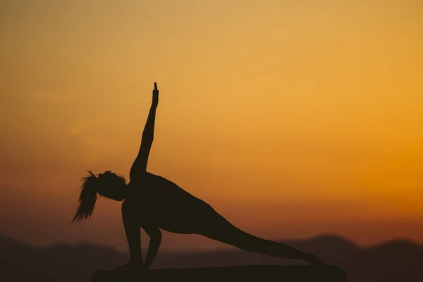 Young woman is practicing yoga on the mountain at sunset. Silhouette of young woman practicing yoga outdoor.