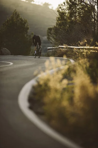 A side shot of a professional slim cyclist riding up a mountain.