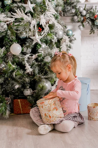 a little girl opens a gift box with Christmas gifts under the Christmas tree
