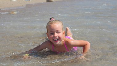 Kız suyun içinde, dalgaların arasında mutlu bir yüzle ve gülümseyerek yatıyor.