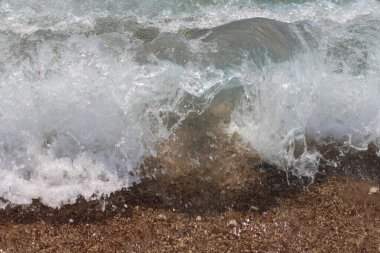 Beyaz tepeli bir deniz dalgası yükselir ve kumlu plaja çarpar. Dalga arkaplan fotoğrafı.