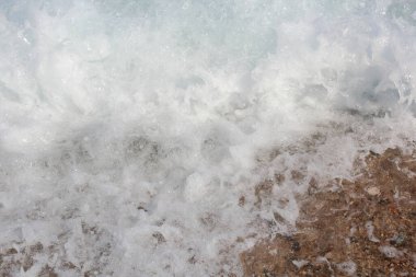 Beyaz tepeli bir deniz dalgası yükselir ve kumlu plaja çarpar. Dalga arkaplan fotoğrafı.
