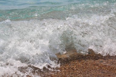 Beyaz tepeli bir deniz dalgası yükselir ve kumlu plaja çarpar. Dalga arkaplan fotoğrafı.