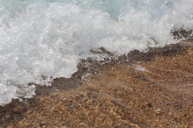 Beyaz tepeli bir deniz dalgası yükselir ve kumlu plaja çarpar. Dalga arkaplan fotoğrafı.